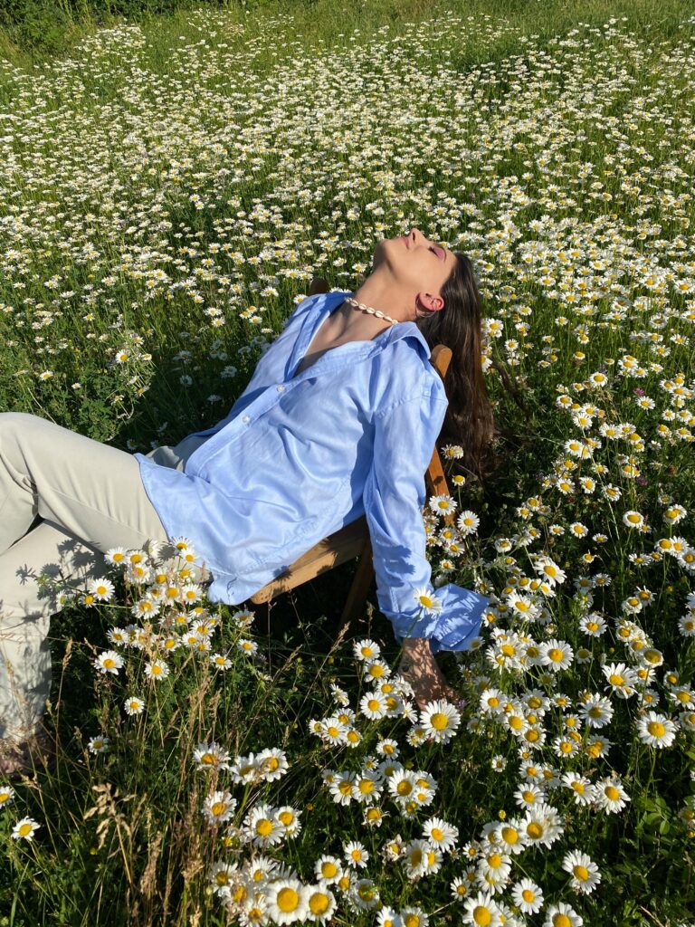 A woman in a blue shirt relaxing in a vibrant chamomile field on a sunny day.